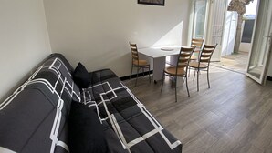 Olohuoneessa on sohva, ruokapöytä tuoleineen, pieni valkoinen pöytä ja liukuovi, joka johtaa ulkotilaan.