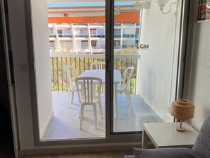 A room with a sliding glass door leading to an outdoor patio with a table and chairs. - Spacious apartment with pool - 6 guests (La Grande-Motte)