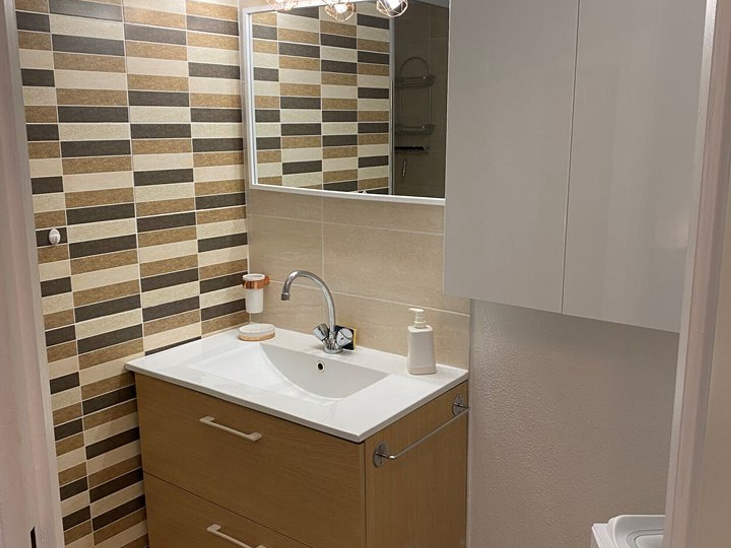 Une salle de bain avec un mur carrelé, un lavabo, un miroir et des meubles en bois.