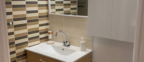 Une salle de bain avec un mur carrelé, un lavabo, un miroir et des meubles en bois.