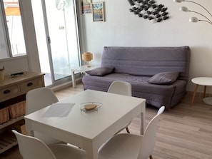 A modern living room with a grey sofa, white chairs, a white table, and a lamp. - Spacious apartment with pool - 6 guests (La Grande-Motte)