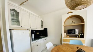 Une cuisine compacte avec des meubles blancs, un réfrigérateur, un four à micro-ondes et une petite table à manger avec une chaise.