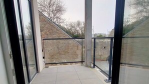 A balcony with a stone wall, glass doors, and a tiled floor. - New apartment in the heart of Le Palais (Le Palais)
