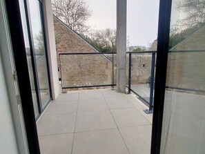 Ein Balkon mit Steinmauer, Glasüren und Fliesenboden.