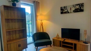 A living room with a wooden cabinet, a green armchair, a wooden coffee table, a TV on a wooden stand, and a painting on the wall. - New apartment in the heart of Le Palais (Le Palais)