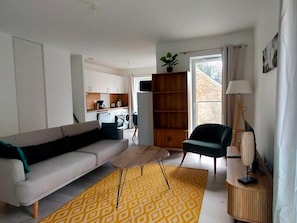 Ein modernes Wohnzimmer mit einer Couch, einem kleinen Couchtisch, einem Sessel, einem Bücherregal und einer Lampe.