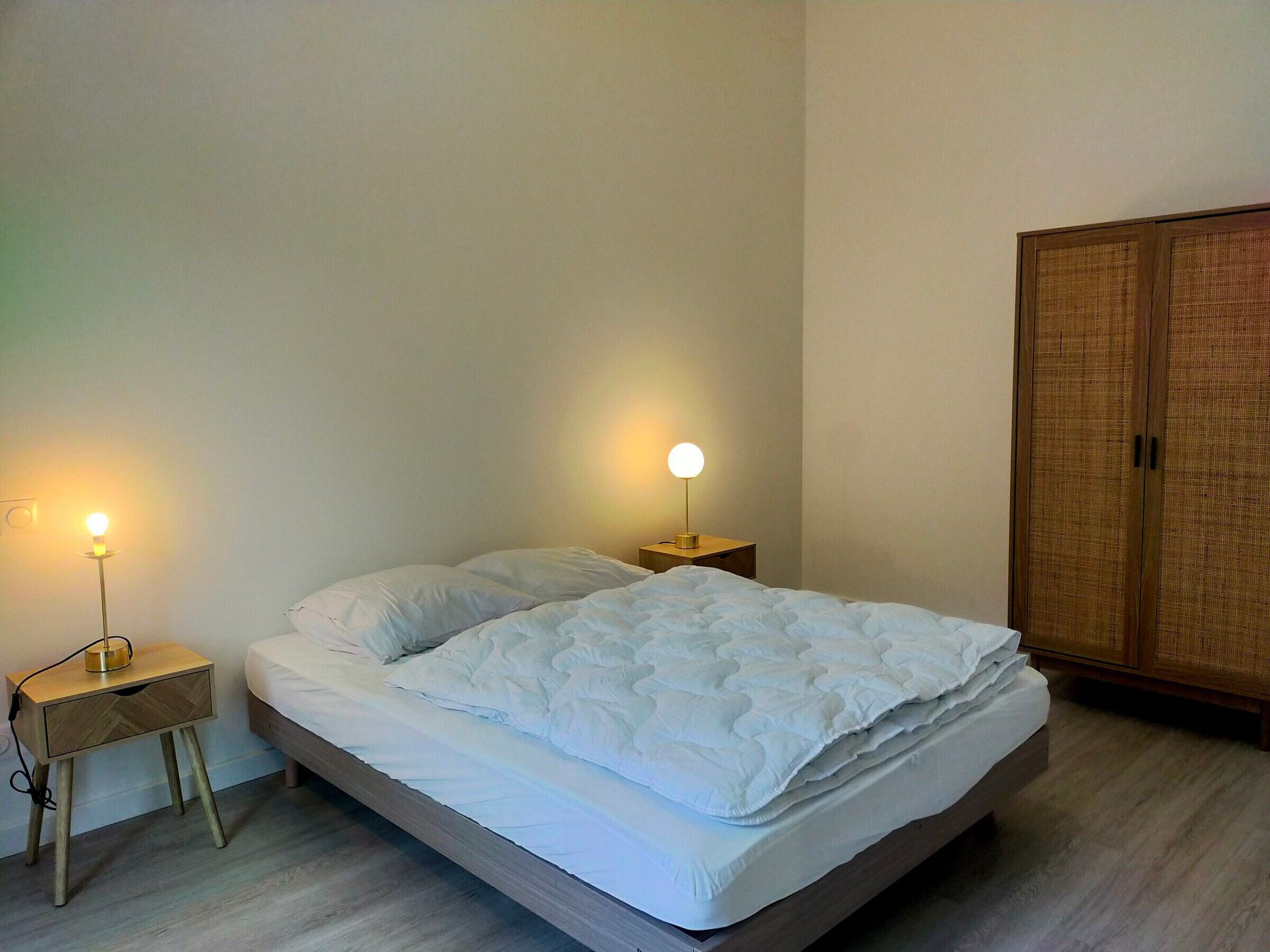 A bedroom with a bed, two bedside tables with lamps, and a wardrobe.