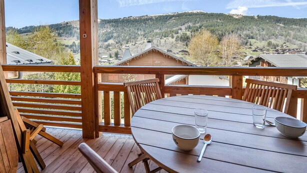 Eine Holzterrasse mit Tisch und Stühlen, mit Blick auf eine gebirgige Landschaft.