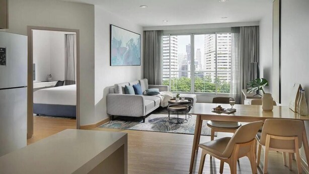 Una sala de estar moderna con sofá, mesa de comedor y sillas, un ventanal con vista a la ciudad y un cuadro en la pared.