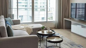 Una sala de estar moderna con un sofá, dos mesas de centro, un televisor y vistas a edificios altos.