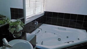 Une salle de bain avec une baignoire blanche, un lavabo et une fenêtre avec des stores.
