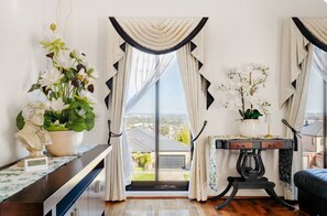 A room with a large window, a bust sculpture, a potted orchid, and a table with a lamp.