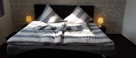 Una cama con ropa de cama a rayas y almohadas, dos lámparas de noche y un fondo de papel tapiz estampado.