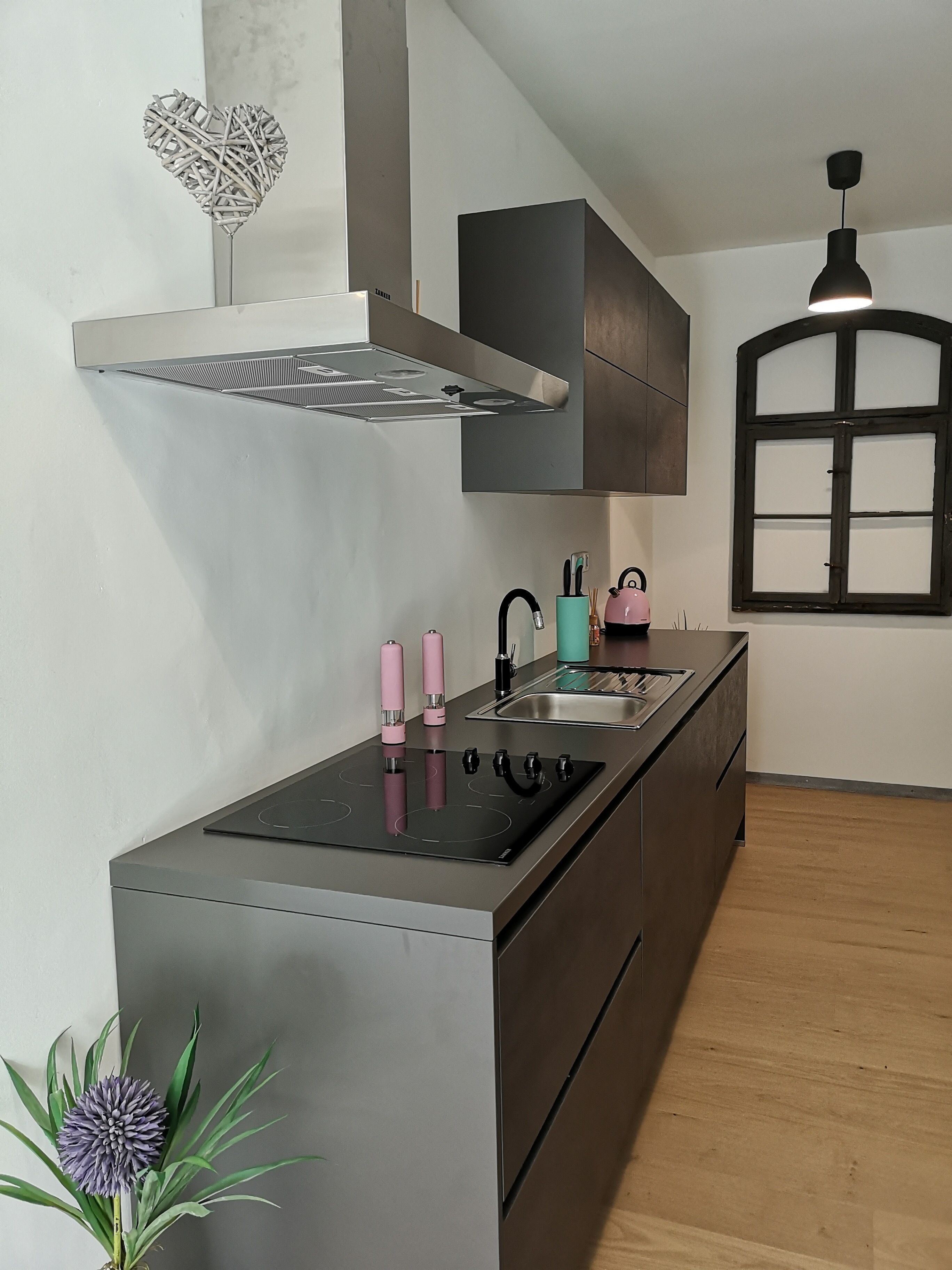 A modern kitchen with a central island, stainless steel appliances, a black range hood, and a window with a dark frame.