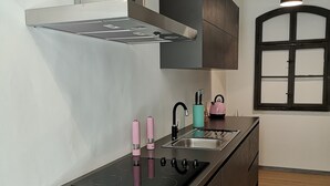 Una cuina moderna amb una illa central, electrodomèstics d'acer inoxidable, una campana extractora negra i una finestra amb marc fosc.