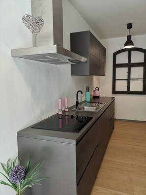 A modern kitchen with a central island, stainless steel appliances, a black range hood, and a window with a dark frame. - Out of the stress, into Zorge - your vacation home awaits (Walkenried)