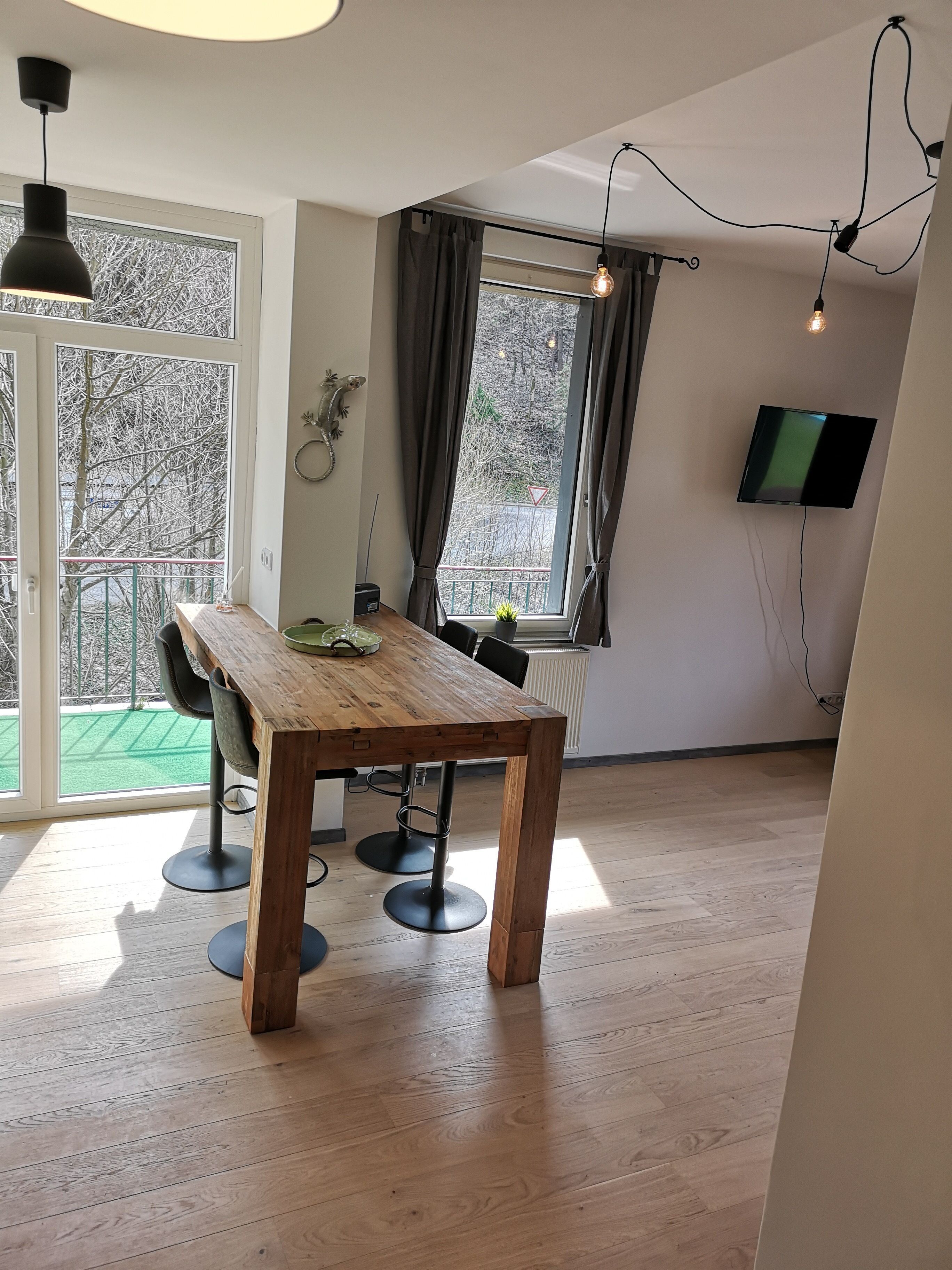 A modern room with a wooden dining table, chairs, a TV mounted on the wall, and a window with curtains.