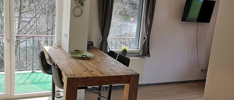 A modern room with a wooden dining table, chairs, a TV mounted on the wall, and a window with curtains.