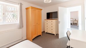 Un dormitorio con cama, armario, cómoda, televisor y puerta que da a otra habitación.