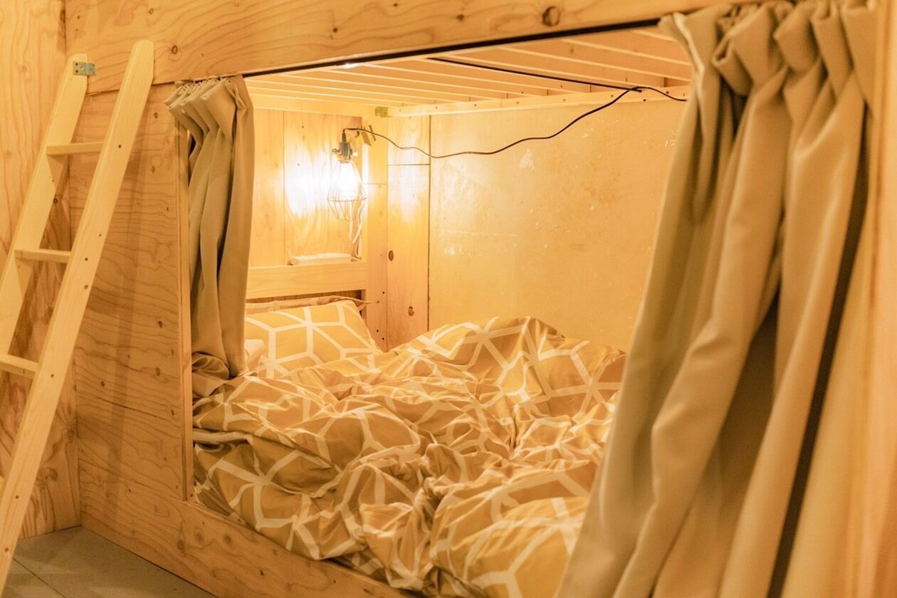 A wooden bunk bed with a ladder, a window with curtains, and a wall-mounted light fixture.
