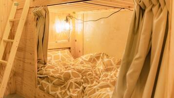 A wooden bunk bed with a ladder, a window with curtains, and a wall-mounted light fixture.