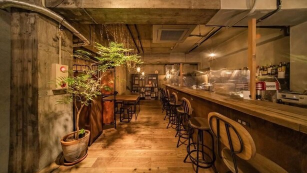 A bar area with wooden flooring, bar stools, and a counter with bottles. - ArtBar & GuestHouse ennova - Hostel (Atami)