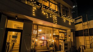 A building with a balcony decorated with string lights, a bench outside, and a signboard. - ArtBar & GuestHouse ennova - Hostel (Atami)
