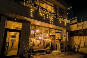 A building with a balcony decorated with string lights, a bench outside, and a signboard.