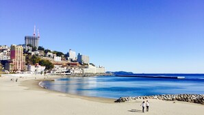 A beach with a cityscape in the background, including a prominent building with a red spire. - ArtBar & GuestHouse ennova - Hostel (Atami)