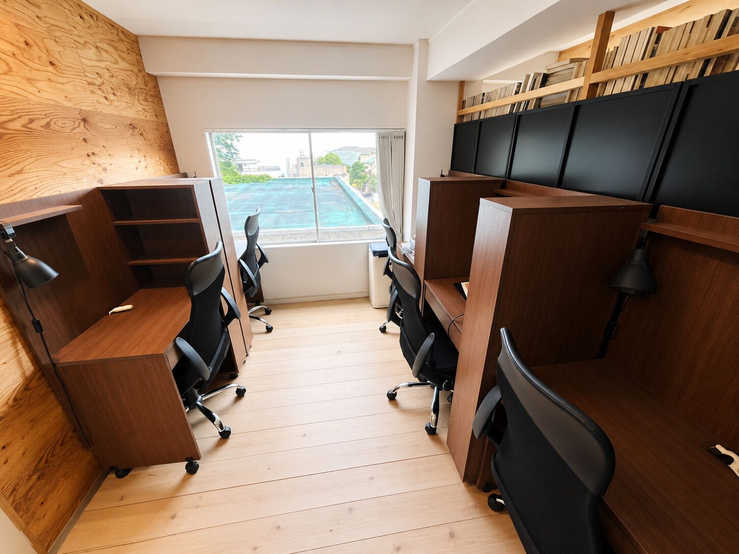 A modern office space with wooden desks, black office chairs, and a view of a swimming pool through a large window.