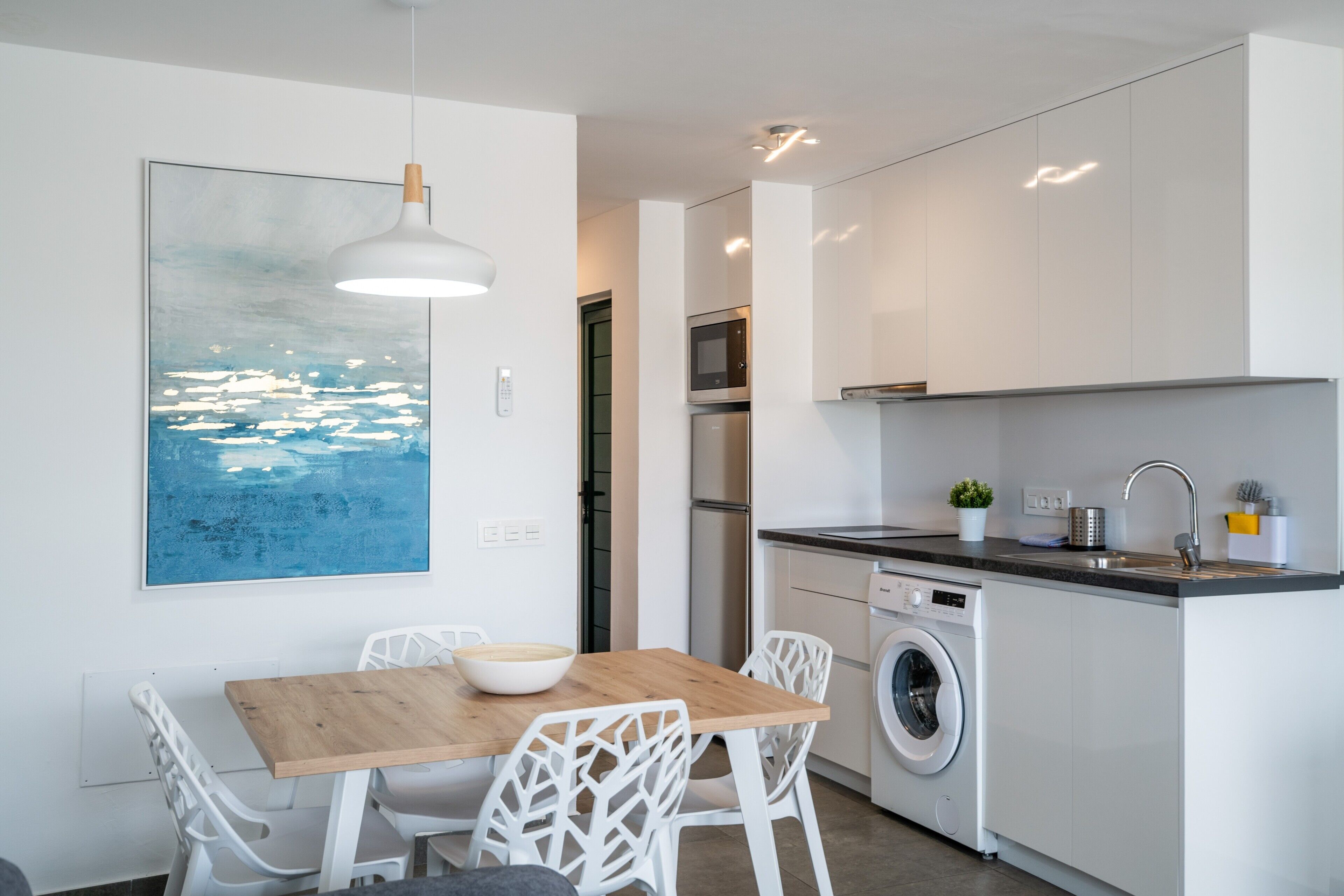 Una cocina moderna con una mesa de comedor, sillas, lavadora y microondas.