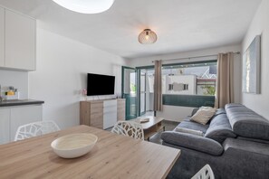 Ein modernes Wohnzimmer mit einer Couch, einem Esstisch mit einer Schüssel, einem Fernseher und Blick ins Freie.
