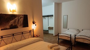 A hotel room with a large bed, two smaller beds, a painting, a wall-mounted light, and a mirror.