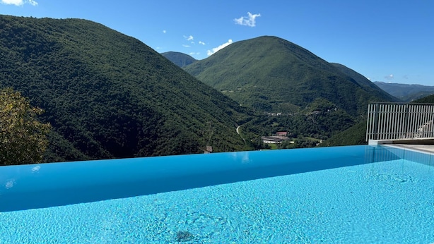 A clear blue pool with a view of lush green mountains and a distant village.