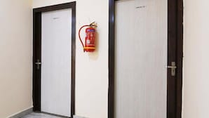 Two closed doors with a fire extinguisher mounted on the wall between them. - Kiya Kedia Niketan Salt Lake (Barasat)