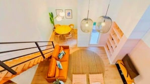 Un ambiente living su più livelli con una scala, un divano, un tavolo da pranzo e lampade a sospensione.