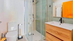 Un bagno con cabina doccia in vetro, un mobile bagno in legno con lavabo e uno specchio sopra il mobile.