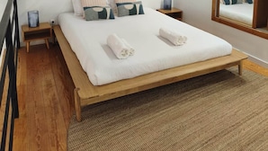 Una camera da letto con un letto di legno, un grande specchio e stampe botaniche incorniciate alle pareti.