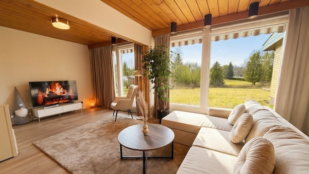 A living room with a sofa, a TV, a fireplace, and large windows. - Relaxing Riverside House with Sauna & Fireplace (Kannus)