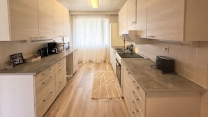 A modern kitchen with light wood cabinets, a central island, and a view of a window with sheer curtains. - Relaxing Riverside House with Sauna & Fireplace (Kannus)