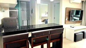 A modern kitchen with a black countertop, a built-in oven, and a TV mounted on the wall. - Apartment for 4 people in Bombas + swimming pools + gym + sauna + games rooms (Bombinhas)