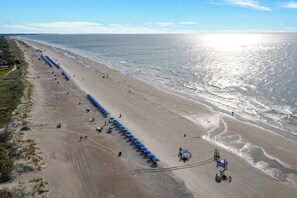 An aerial view of a beach with rows of blue umbrellas and beach chairs, a sandy shoreline, and the ocean in the background. - Spacious and modern 3 bedroom villa with stunning lagoon views (Hilton Head Island)