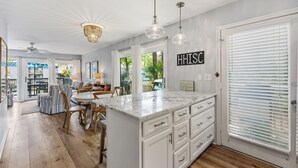 A modern kitchen with a marble island, pendant lights, and a view of the outdoors. - Spacious and modern 3 bedroom villa with stunning lagoon views (Hilton Head Island)