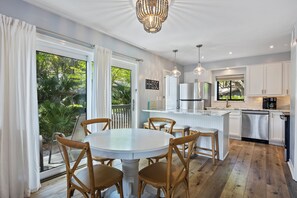 Une cuisine moderne avec des meubles blancs, un réfrigérateur en acier inoxydable et un coin repas comprenant une table ronde et des chaises en bois.