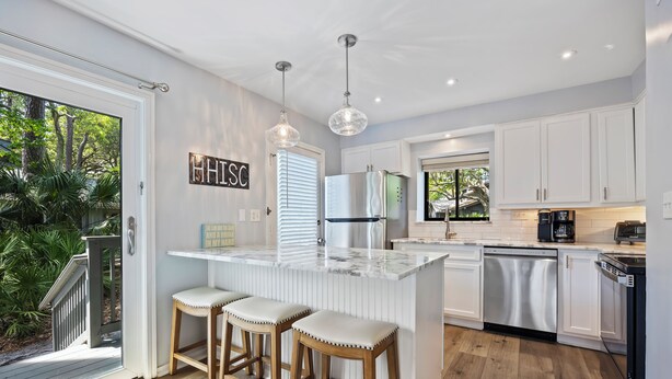 A kitchen with white cabinets, a stainless steel refrigerator, a dishwasher, and a bar stool area. - Spacious and modern 3 bedroom villa with stunning lagoon views (Hilton Head Island)