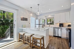 A kitchen with white cabinets, a stainless steel refrigerator, a dishwasher, and a bar stool area. - Spacious and modern 3 bedroom villa with stunning lagoon views (Hilton Head Island)