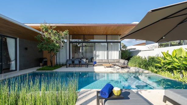 A modern outdoor pool area with a wooden pergola, a seating area, and a dining setup. - Villa Kaya (Thep Krasattri)