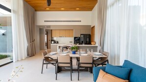 A modern dining area with a table set for six, a blue sofa, and a kitchen in the background. - Villa Kaya (Thep Krasattri)