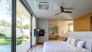 A modern bedroom with a large bed, a television, and a view of a swimming pool. - Villa Kaya (Thep Krasattri)