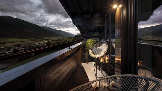 Ein Balkon mit Blick auf Gleise und Berge, ein Korbstuhl und ein kleiner Tisch mit Kerzen.